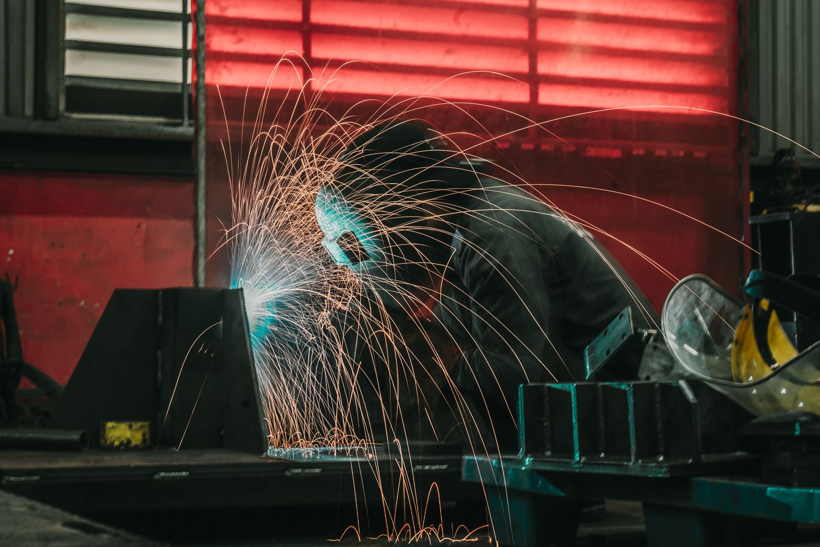 Soldador com máscara de proteção a soldar metal em oficina